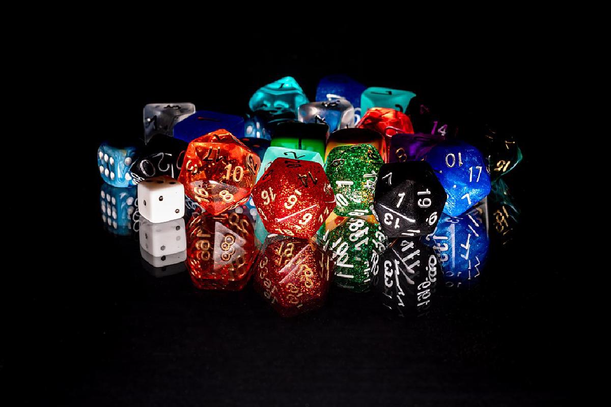 Eine bunte Auswahl an verschiedenen Würfeln auf schwarzer spiegelnder Oberfläche.
