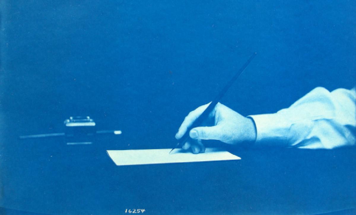 Eine blaue gebleichte Fotography eines Arms der von Rechts in das Bild hineinreicht, in einem weißen Hemdsärmel steckt und einen Federfüller in der Hand hält und kurz davor ist ein weißes Blatt zu behrüren.